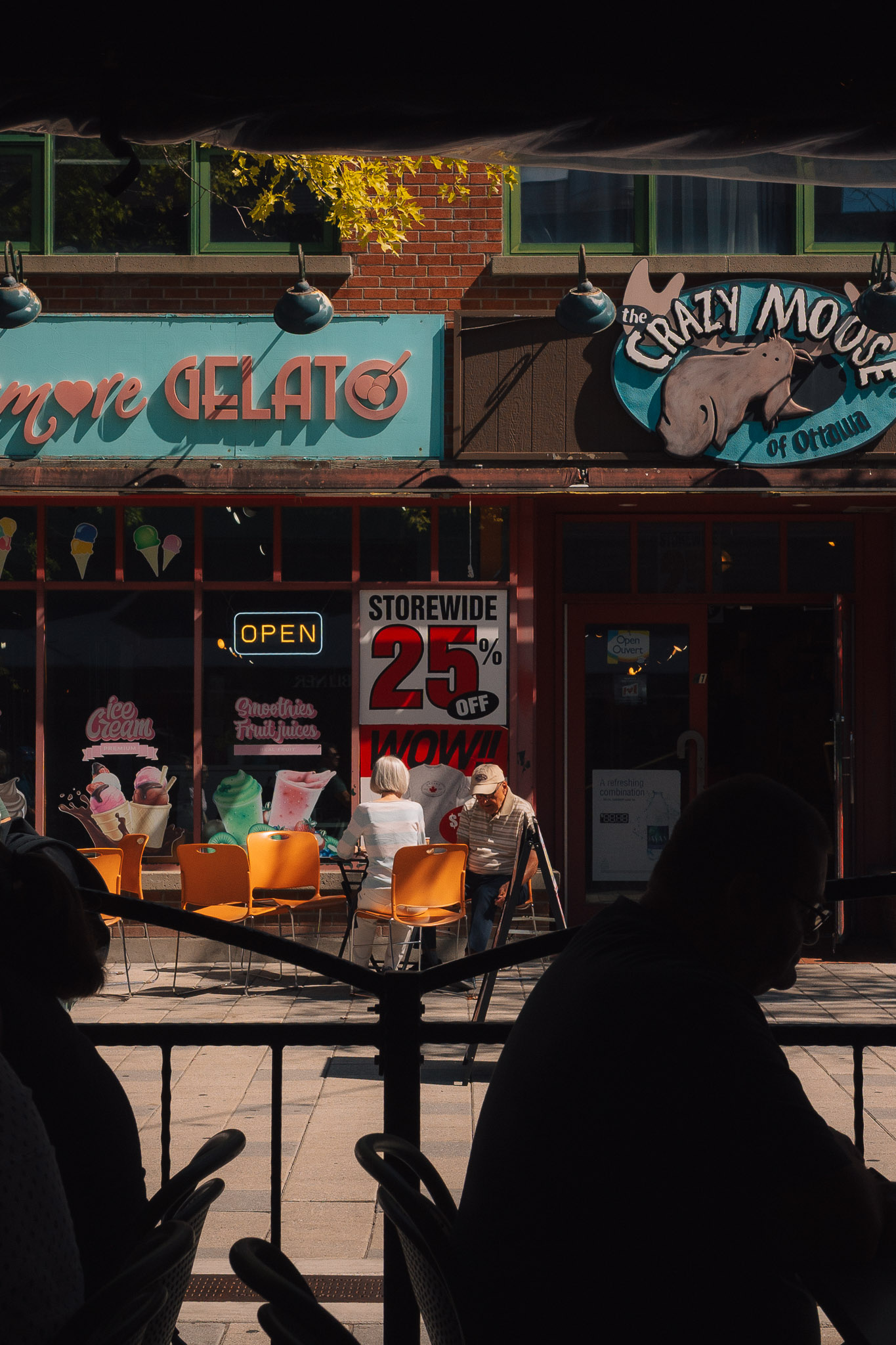 Gelato shop and its patio seen past the dark silhouettes of people in the foreground