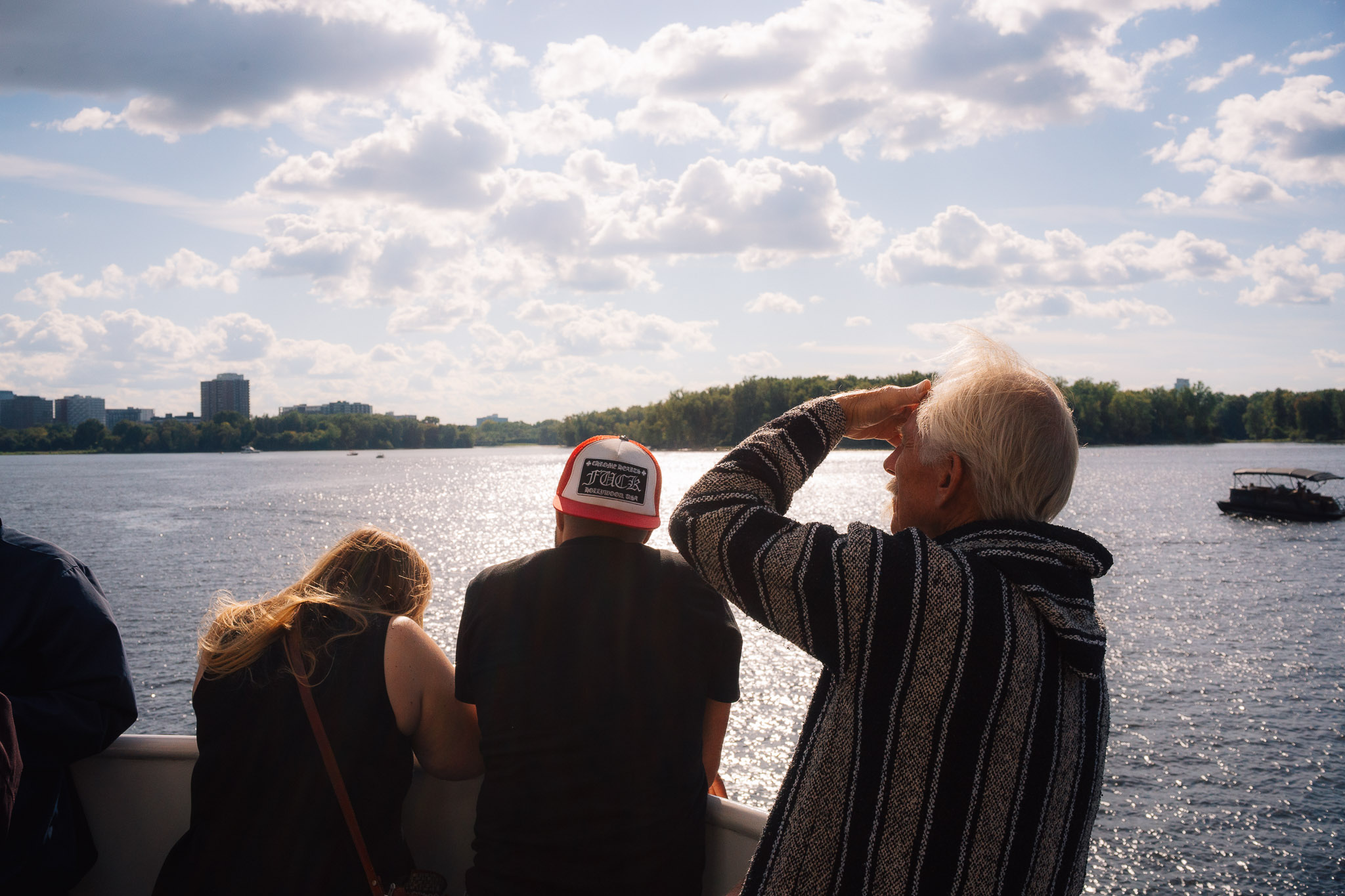 Man shielding his eyes from the sun beside passengers at a boat railing