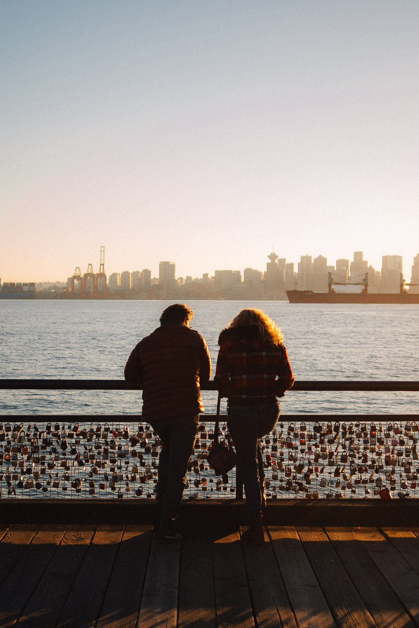 Couple leaning on a railing covered in love locks, watching the city skyline at sunset