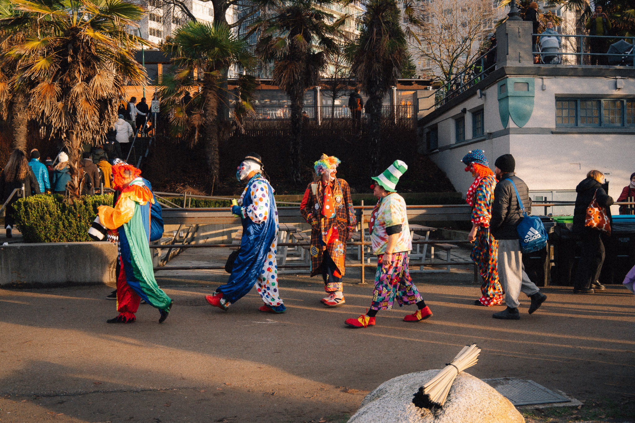 Line of people in colourful clown costumes walking along a waterfront path