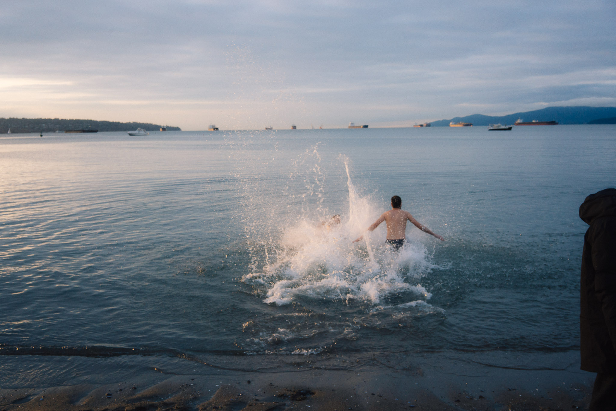 Swimmer running into the cold sea in a burst of spray at dusk