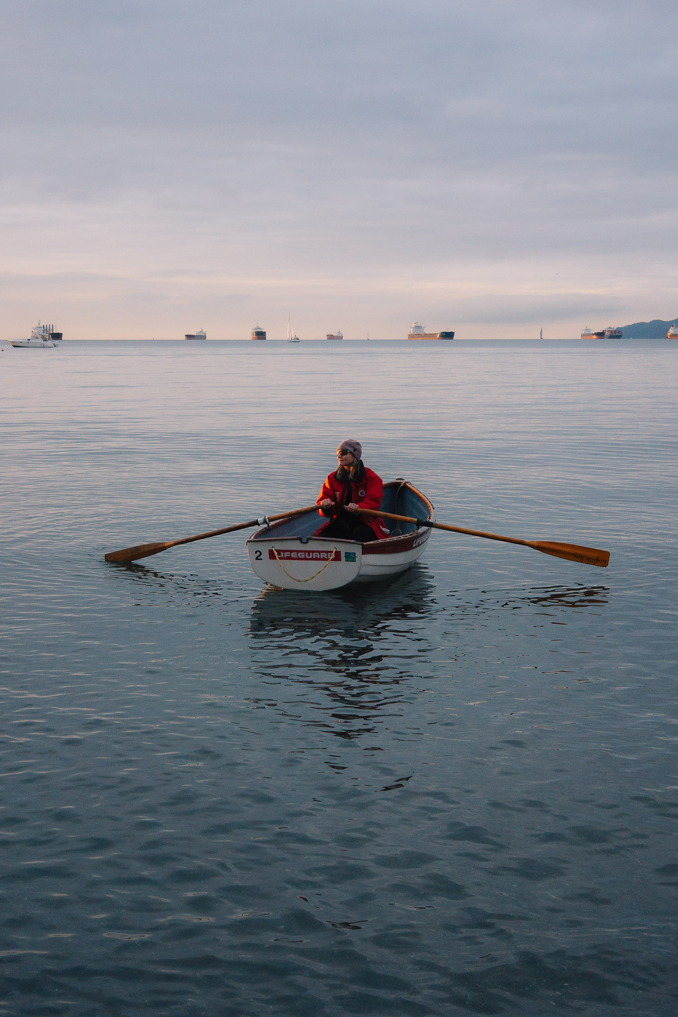 Lifeguard in a red jacket rowing a small boat on calm grey water