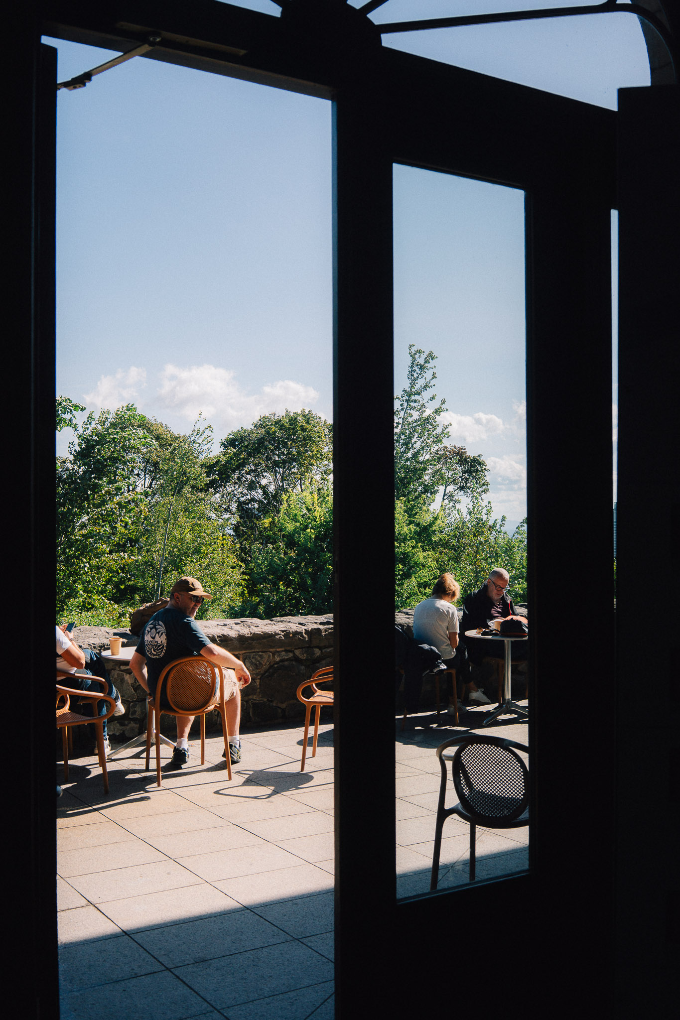 Café terrace seen through the frame of an open door, people sitting in the sun