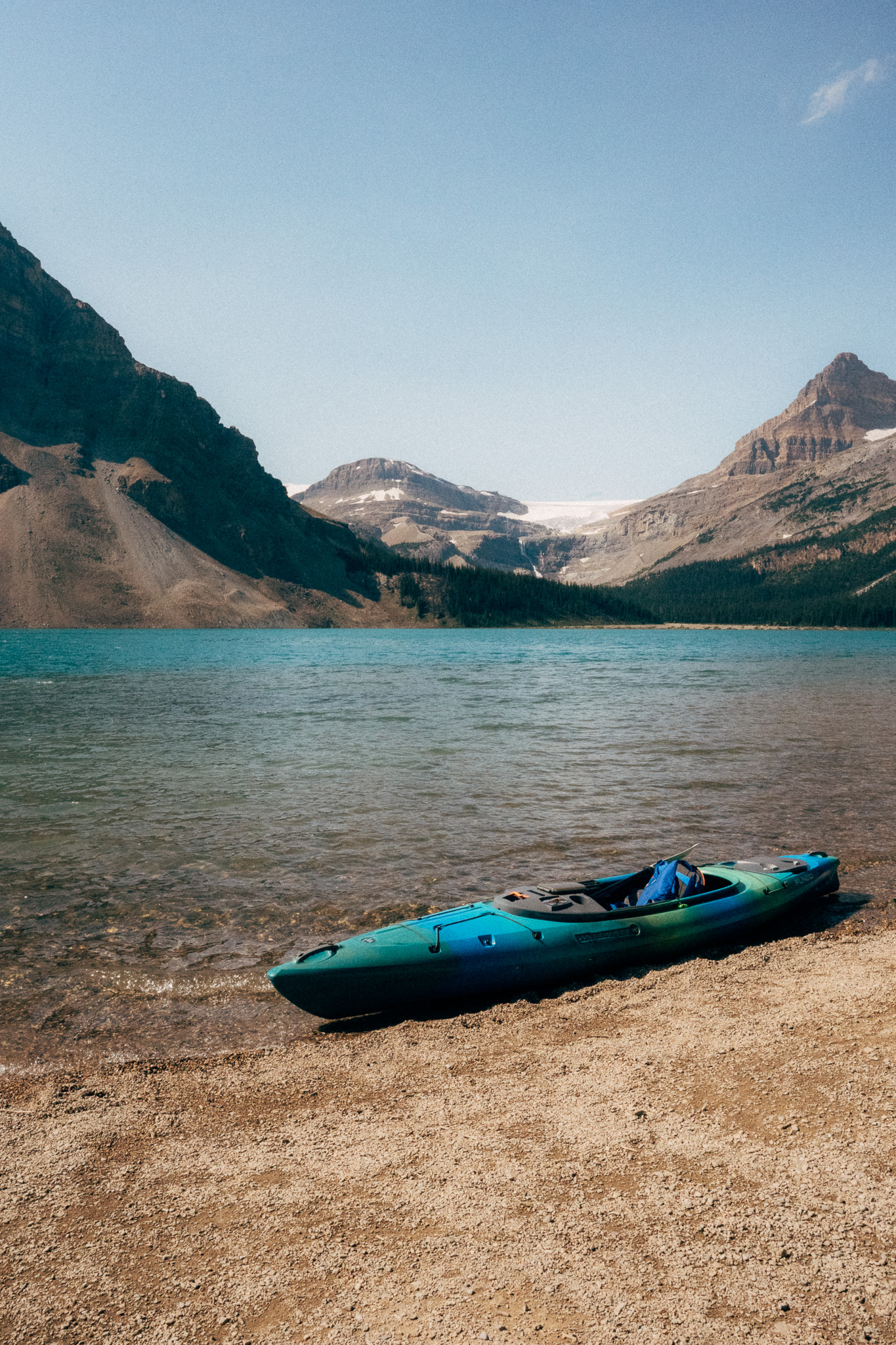 Teal kayak beached on the gravel shore of a glacial lake
