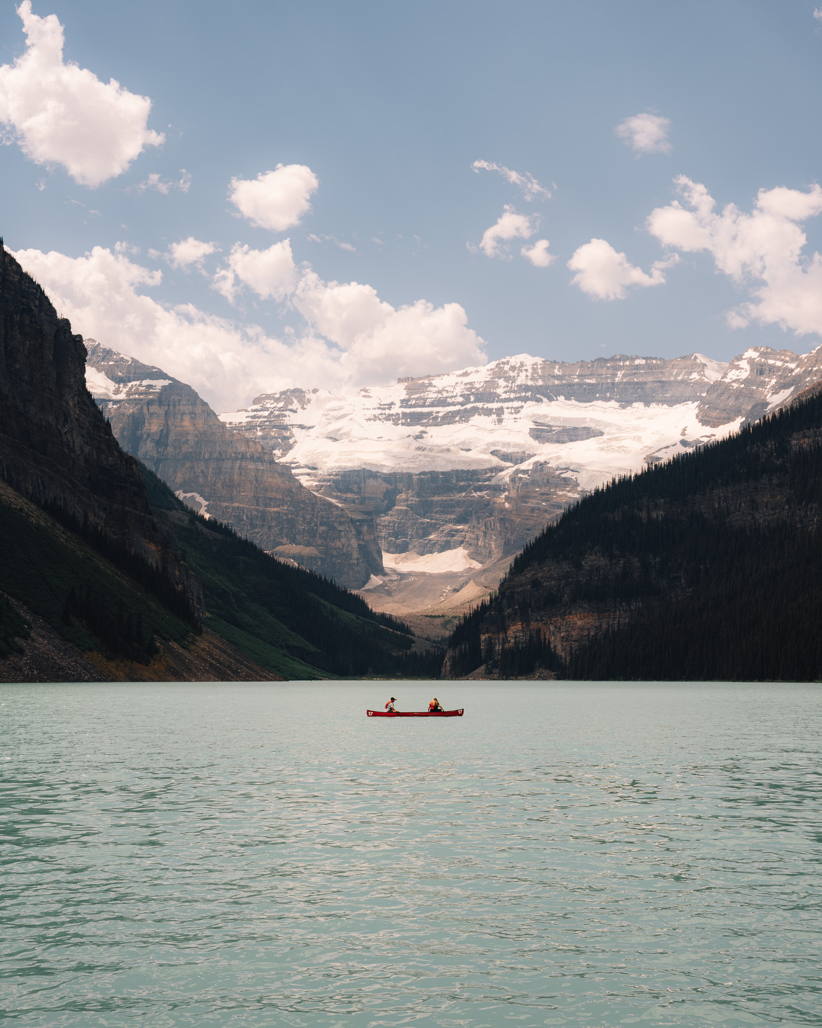 Red canoe crossing a turquoise lake below a glacier headwall