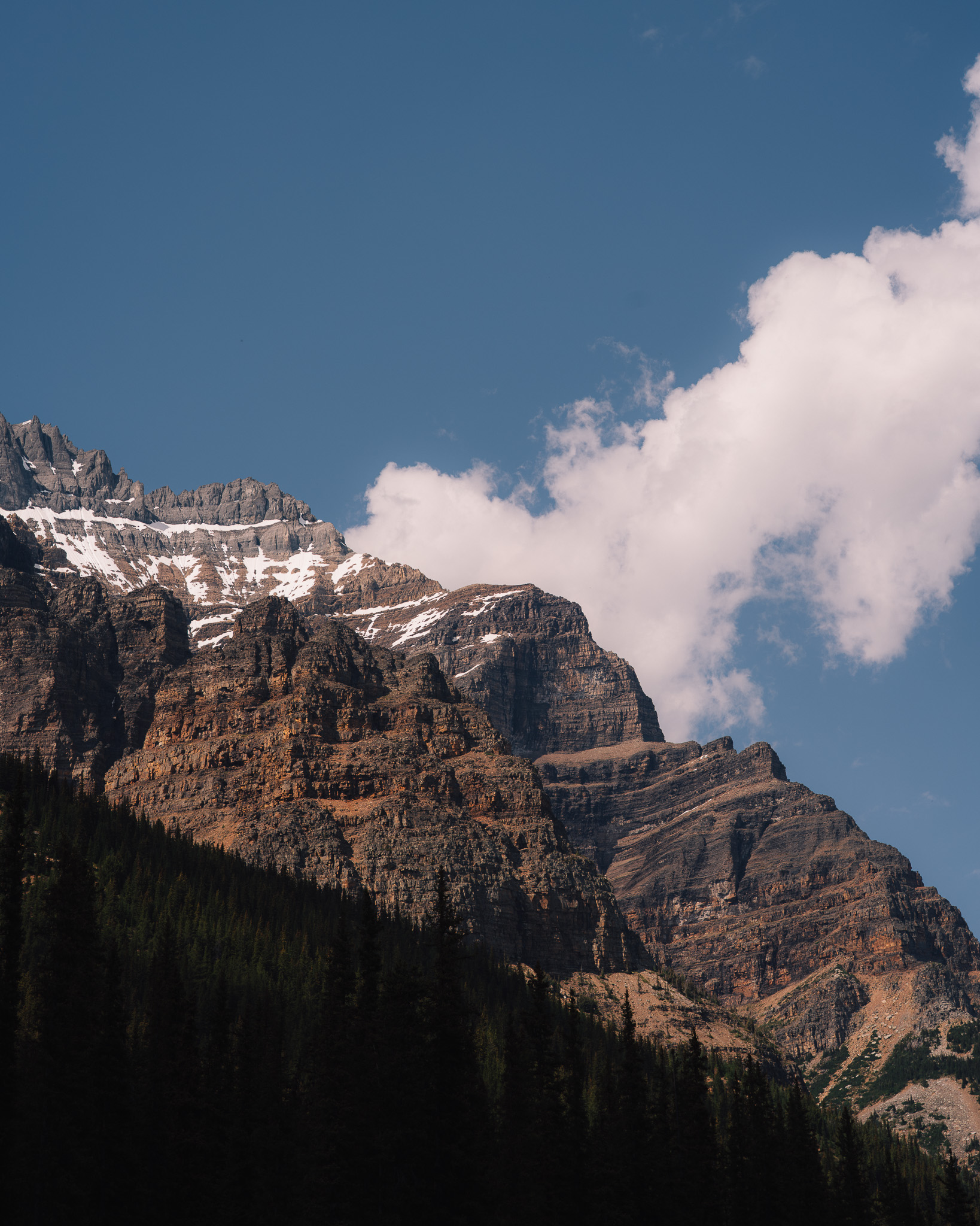 Layered cliff face capped with snow beside a single white cloud