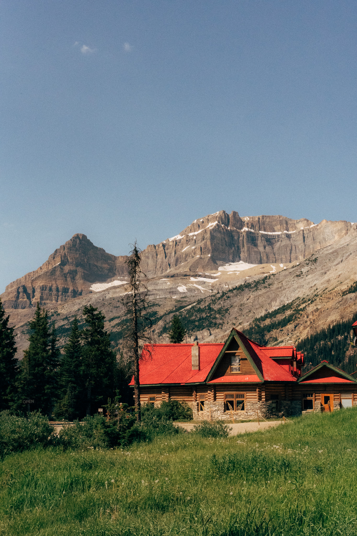 Red-roofed log lodge in a meadow beneath a mountain wall