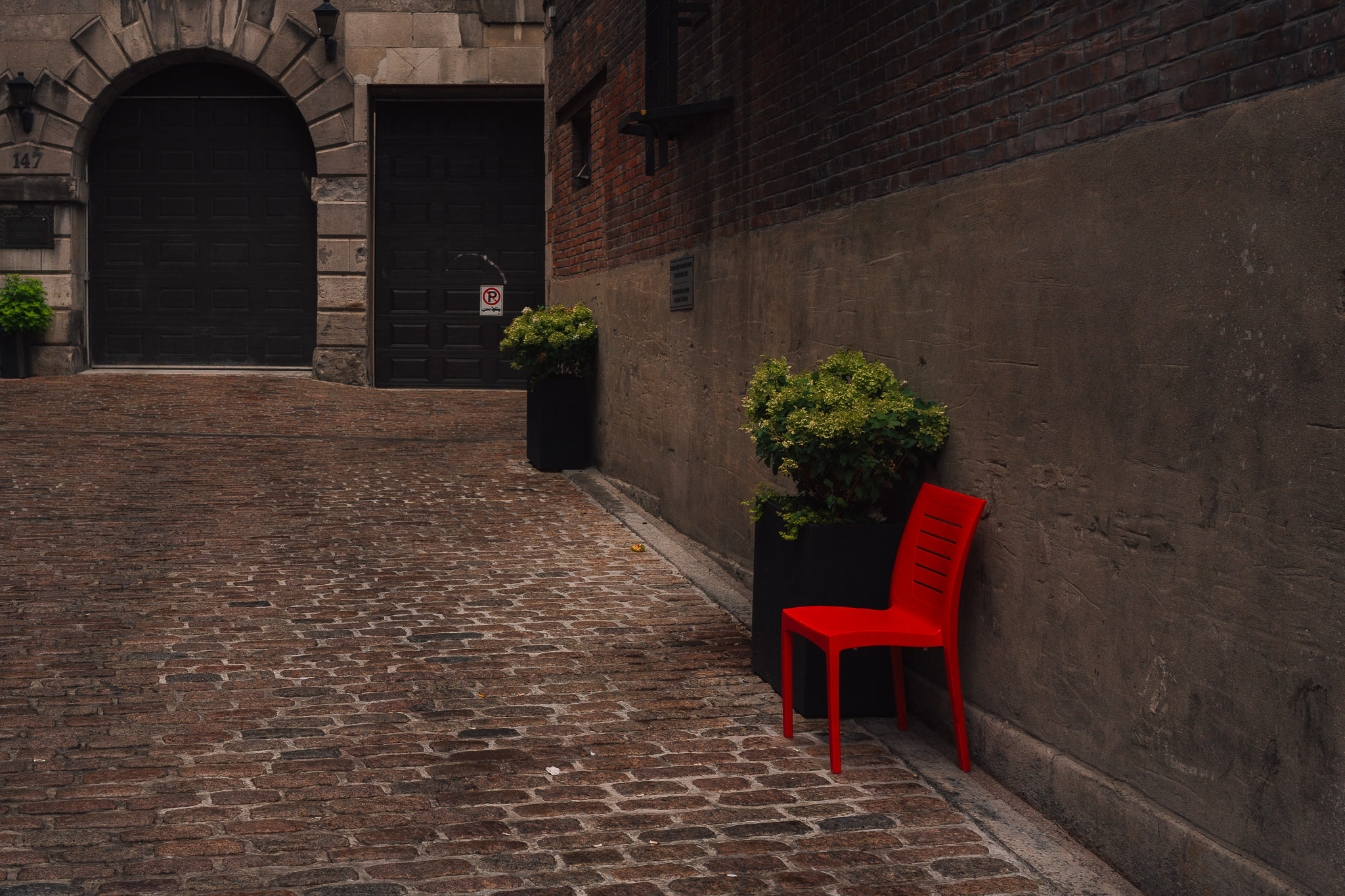 Single red chair against a stone wall in a cobblestone courtyard