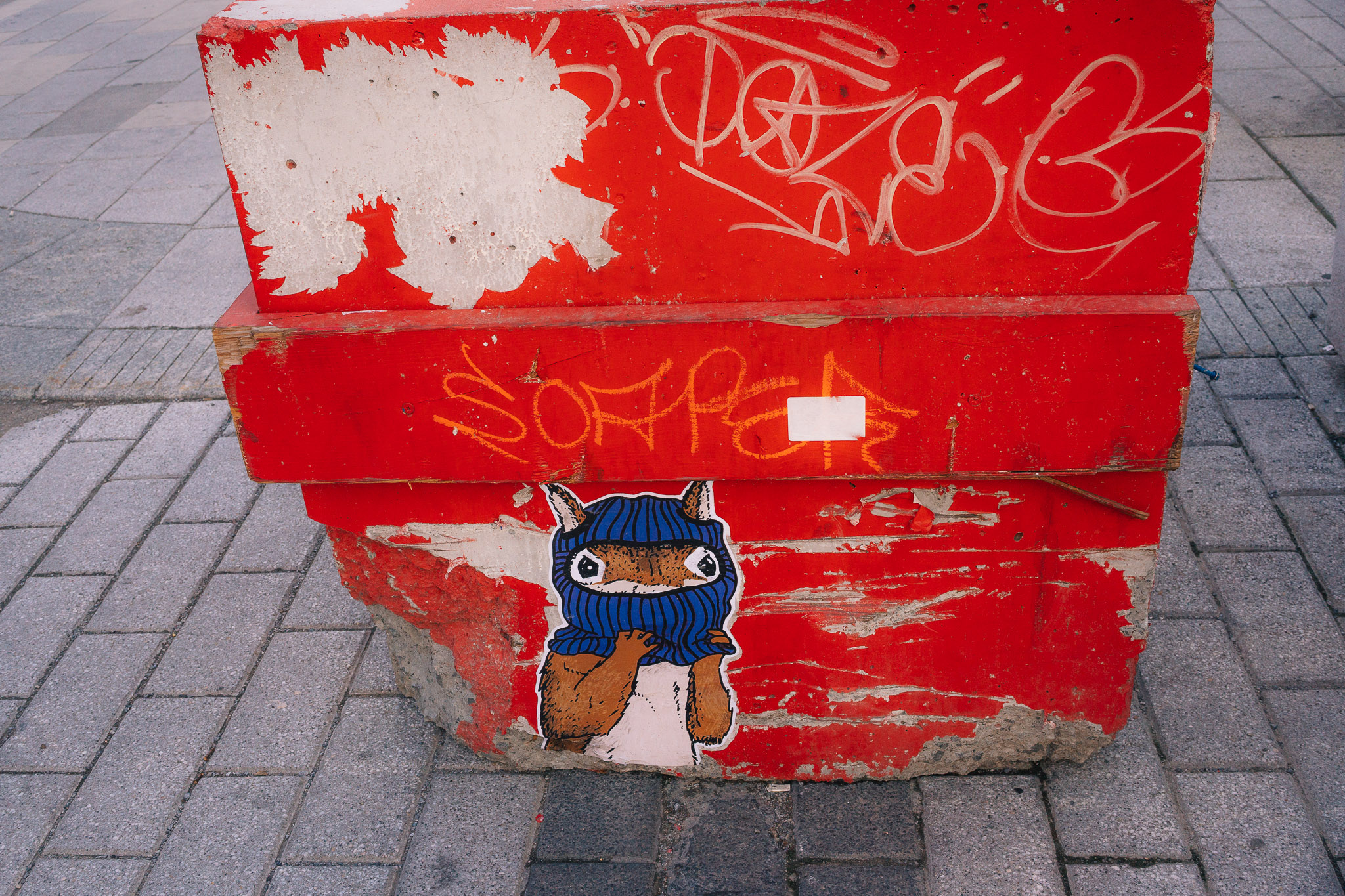 Red concrete barrier covered in graffiti and a sticker of a small blue creature