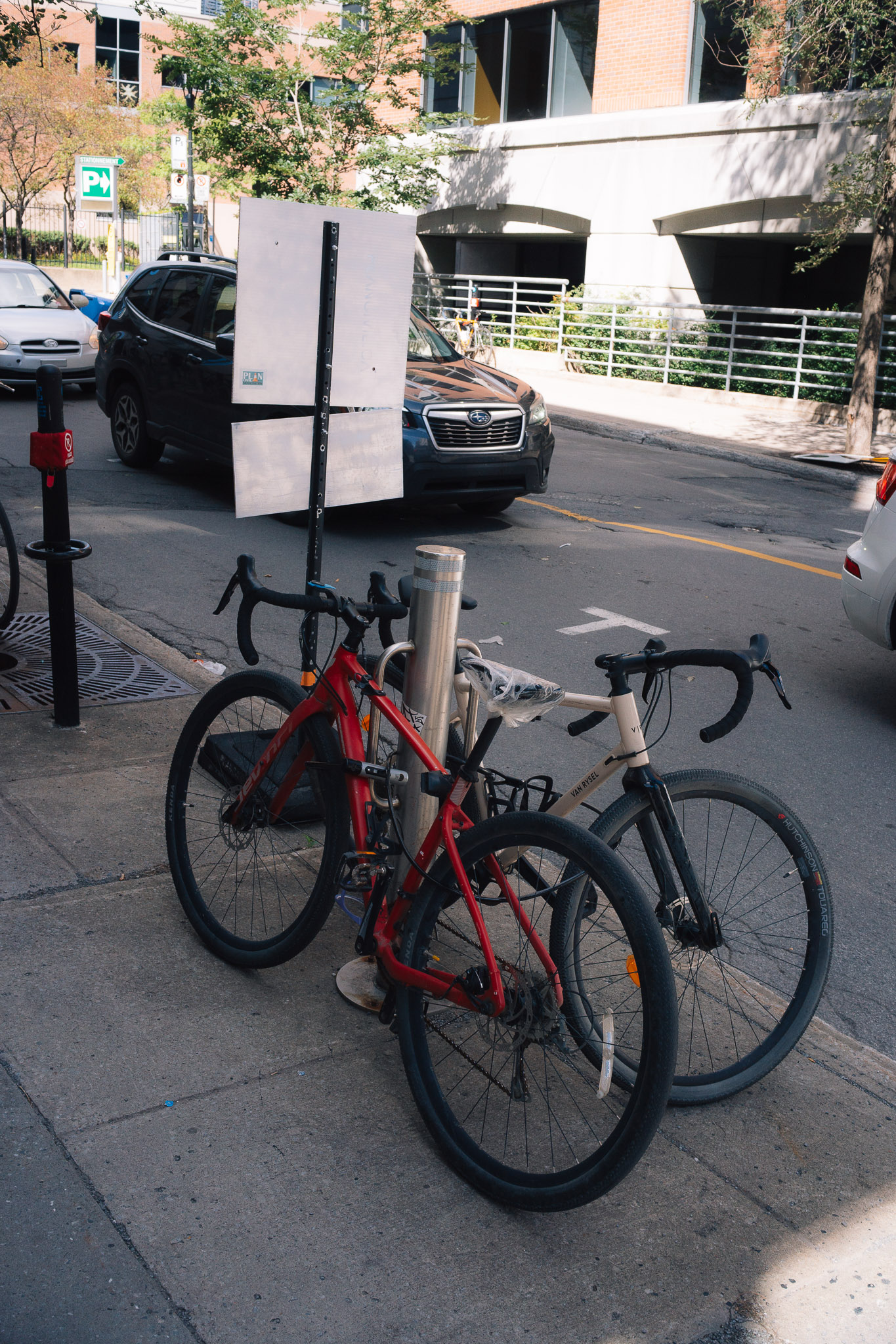 Red road bike locked to a post beside a white bike on a quiet sidewalk