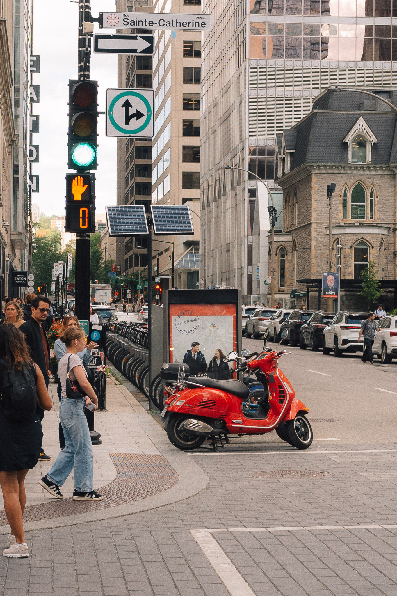 Red scooter parked at a busy downtown corner as pedestrians wait to cross