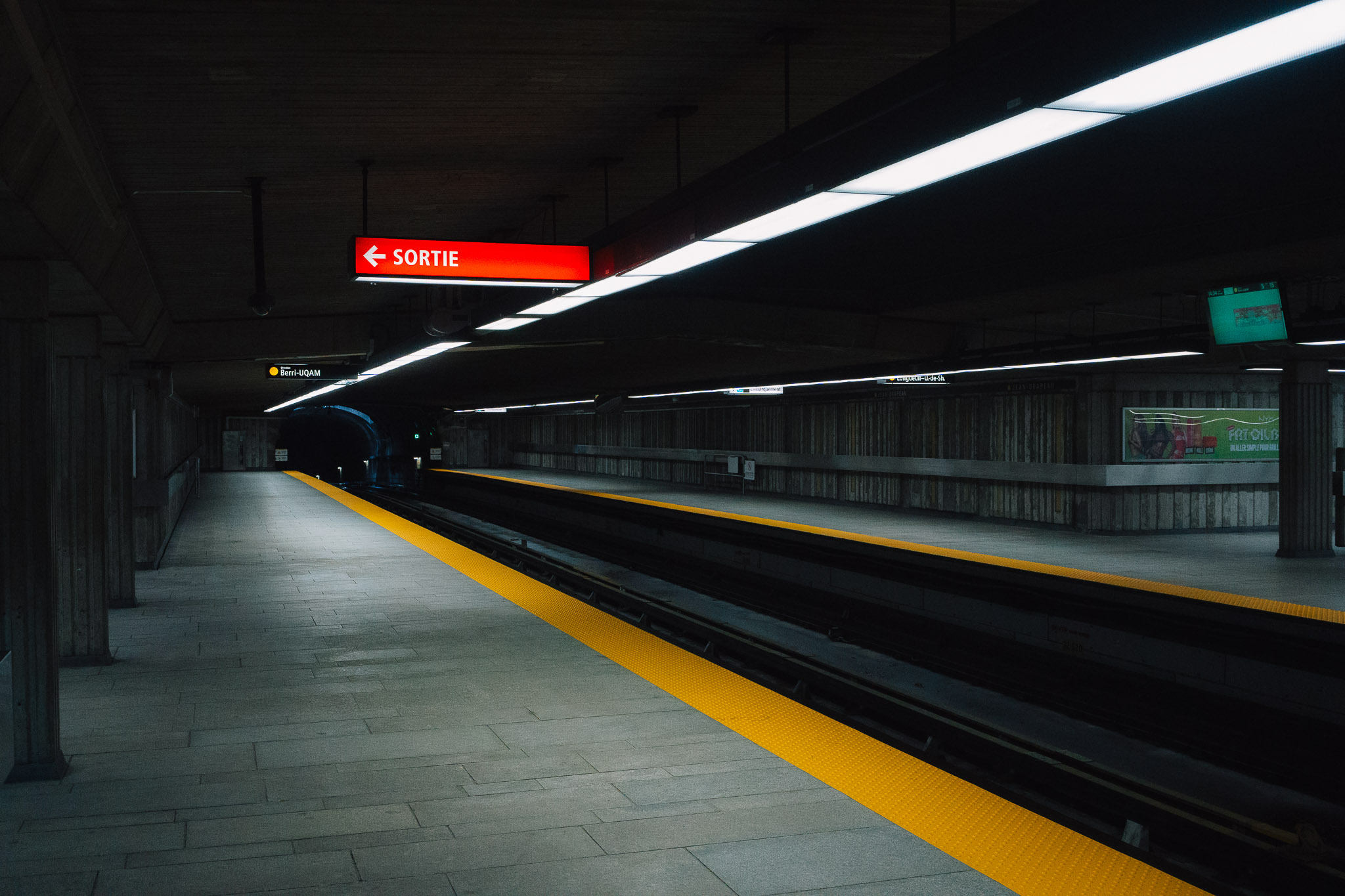 Empty metro platform with a red sortie sign glowing under long ceiling lights